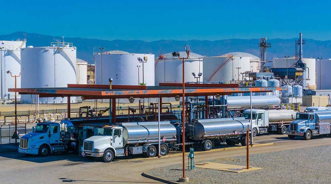 Fuel tanker trucks stationed at an oil refinery with large storage tanks in the background, highlighting the transportation and distribution process in the petroleum industry.